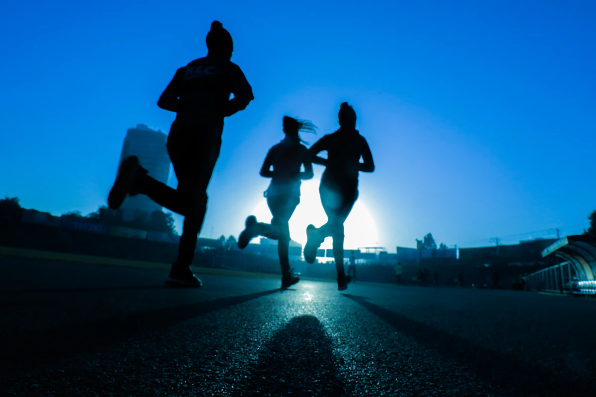 Trois coureurs à contre-jour sur une route, juste avant le lever du soleil